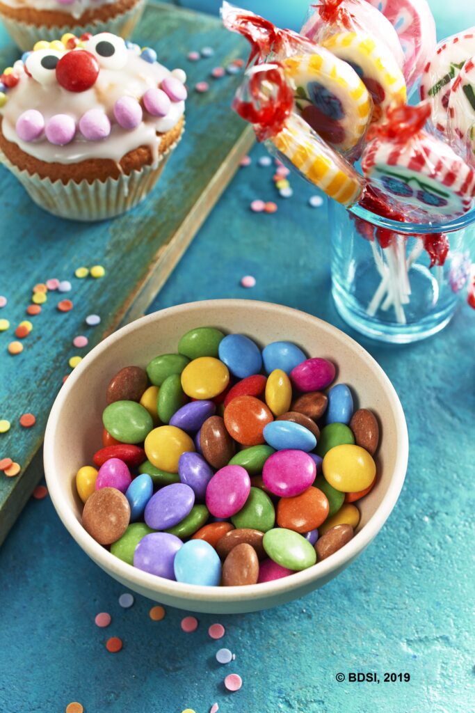 Neben Narren-Muffins, Kreppel & Co. kann man auch ein Glas mit bunten Bonbons oder knallige Lollis auf den Tisch stellen. Das bringt zusätzlich Farbe auf die Tafel.